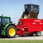 en grønn traktor med en foringsblander og en silograbb som heller for i blanderen