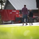 en mann og en gutt holder hender og ser på en rød traktor med forblander bak